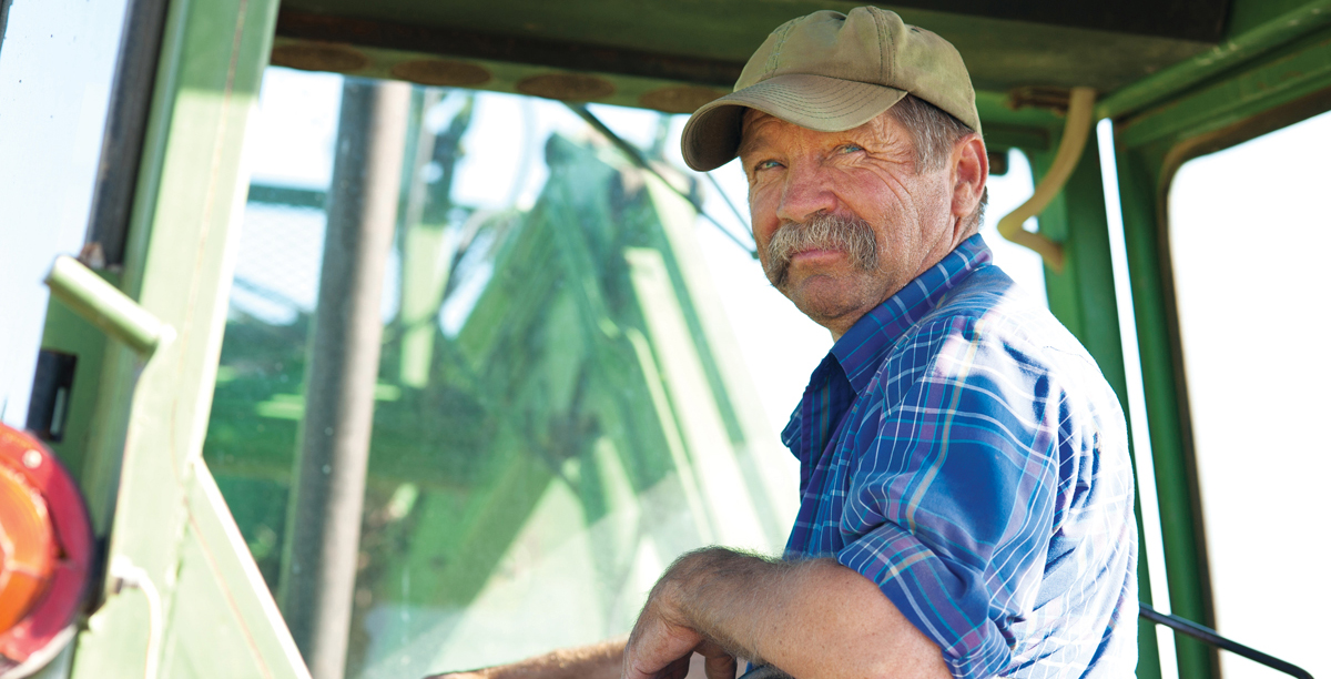 A candid portrait of a senior male farmer sitting in a green tractor.