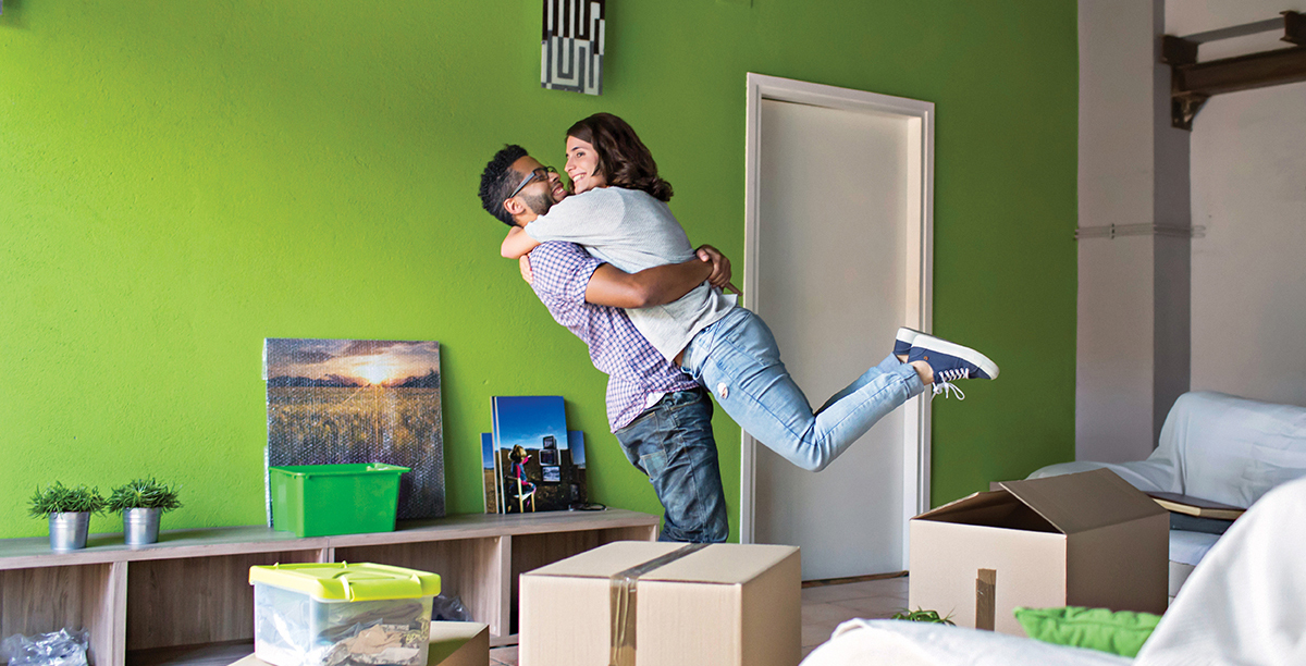 Couple celebrating moving to their new home surrounded by cardboard boxes.